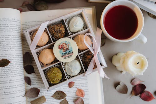 grátis Caixa de doces variados e xícara de chá de cravo em um ambiente aconchegante com livro aberto. Foto profissional